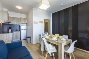 A modern kitchen with a coffee maker, refrigerator, and wooden cabinets. There is a dining area with a table set for four, chairs, and a large window.