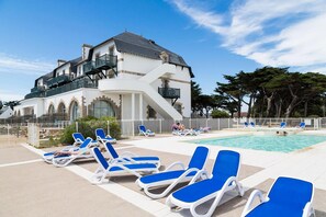 A pool area with lounge chairs and a large building with a balcony.