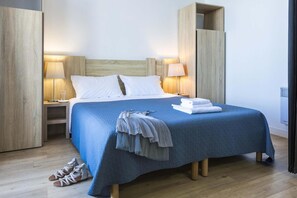 Quarto de hotel com cama, abajures, mesa de cabeceira, um par de sapatos e uma toalha.
