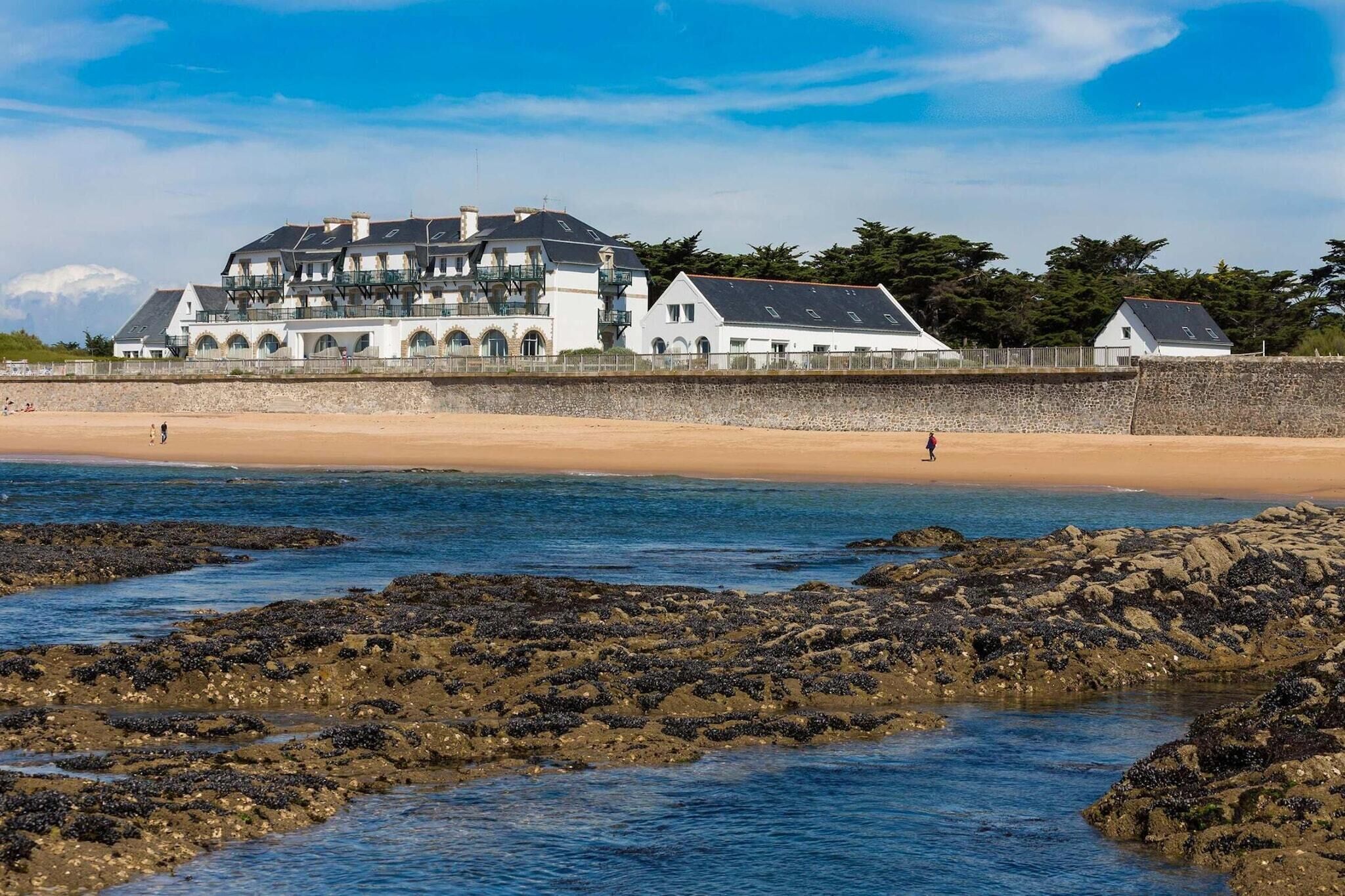 A coastal building with multiple balconies, a sandy beach, and rocky shoreline.