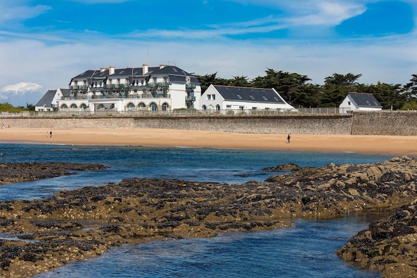 A coastal building with multiple balconies, a sandy beach, and rocky shoreline.