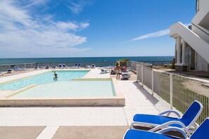 Uma área de piscina com duas piscinas, espreguiçadeiras e vista para o mar.
