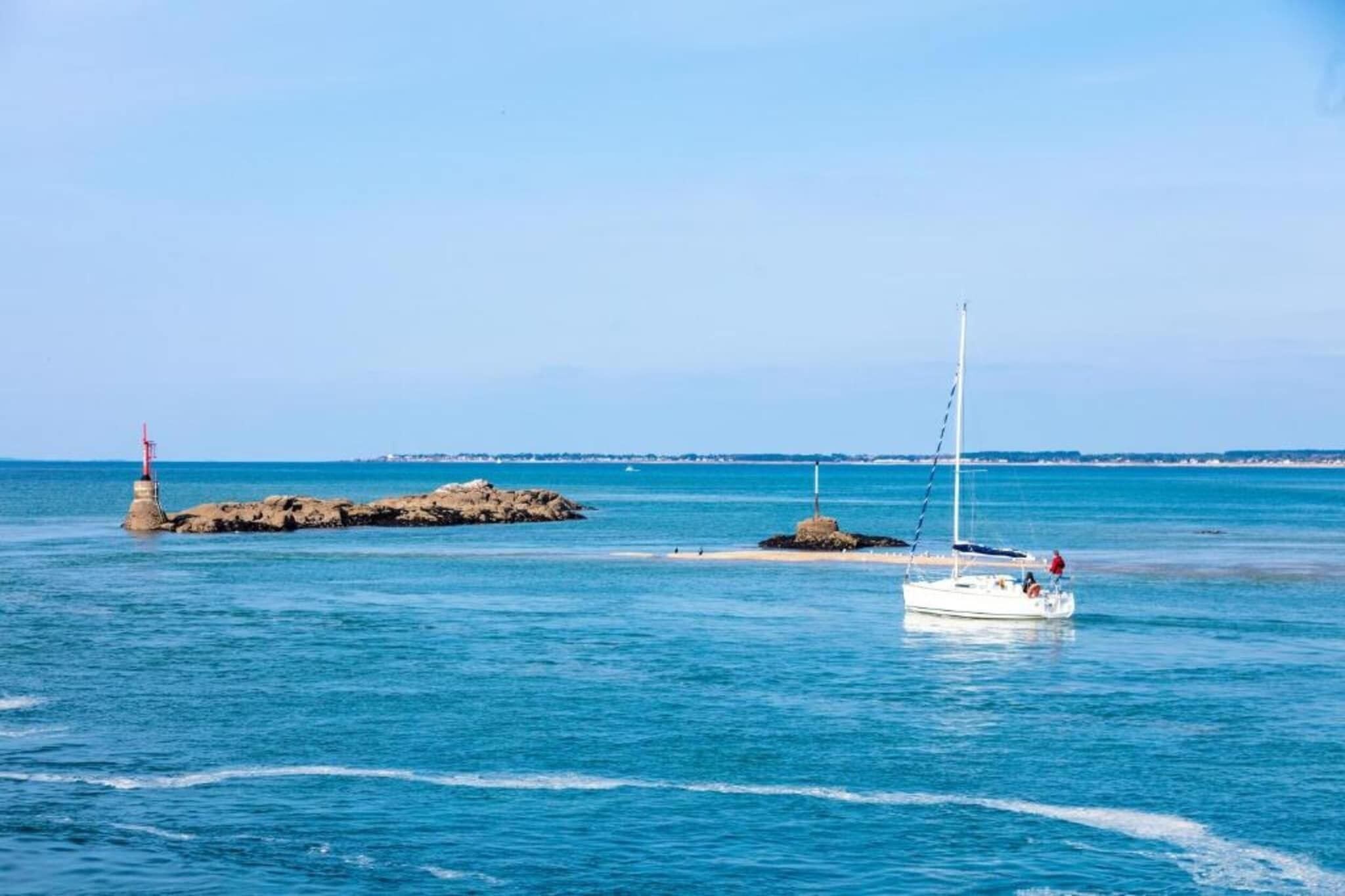 A calm sea with a sailboat and a lighthouse in the distance.