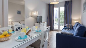 Moderni hotellihuone, jossa on ruokailutila, sohva ja parveke, jossa on verhot.