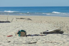 A beach with scattered items including a bag, a blanket, and a surfboard.