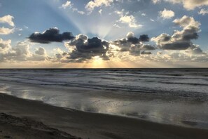 A beach with waves, a sandy shore, and a partly cloudy sky with sunlight.