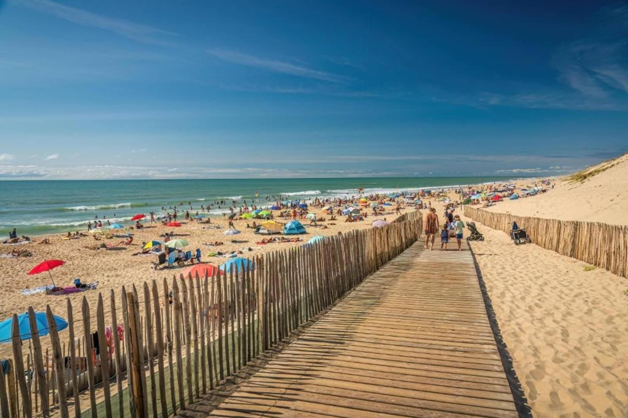 A wooden boardwalk leading to a sandy beach with umbrellas and people.