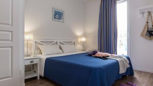 Een slaapkamer met een bed, nachtlampjes, een raam met gordijnen en een deur.