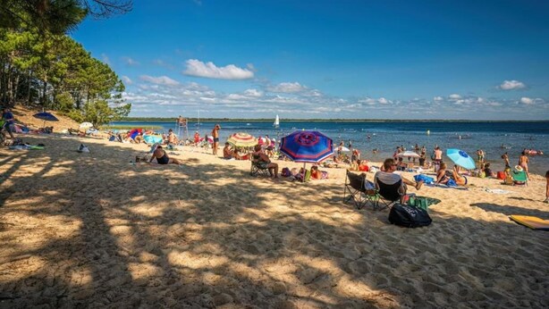 Een strand met mensen die zonnebaden, parasols en een zeilboot in de verte.