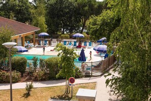 A swimming pool area with lounge chairs and umbrellas, surrounded by trees and a fenced poolside. - Maisonette by Hourtin-Carcans Lake (Hourtin)