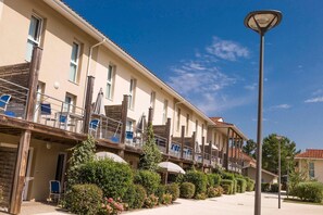Un hotel de varios pisos con balcones, asientos exteriores y cielo despejado.