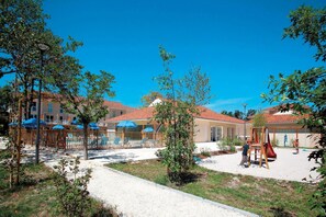 Un patio con un parque infantil, mobiliario exterior y un edificio con tejado de baldosas.