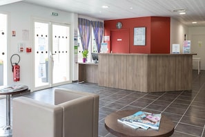 A reception area with a wooden counter, a fire extinguisher, a clock, and a seating area with a magazine on a table.