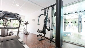 Een sportschool met cardioapparatuur, een krachttrainingapparaat en uitzicht op buiten.