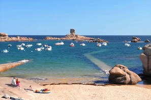 A beach with boats in the water, rocky formations, and people on the sand.