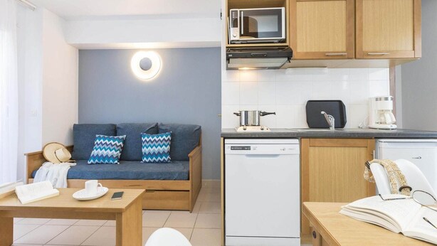 A compact living space with a kitchenette, a sofa with patterned cushions, a dining table, and a coffee machine. - Apartment in Trégastel near the Beach (Trégastel)
