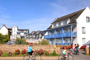 Eine Wohnstraße mit Häusern, einer Mauer aus Stein mit Blumen und Radfahrern.