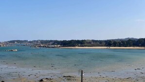 A coastal landscape with clear water, a sandy beach, and a distant hill with vegetation. - Apartment in Trégastel near the Beach (Trégastel)