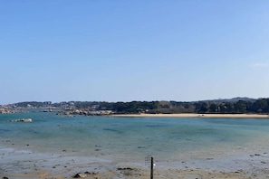 Eine Küstenlandschaft mit klarem Wasser, einem Sandstrand und einer in der Ferne liegenden, bewachsenen Hügel.