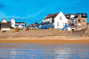 A coastal residential area with houses, some with balconies, and a sandy beach in the foreground.