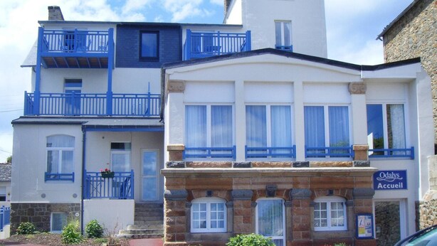 Ein mehrstöckiges Gebäude mit blauem Balkon, einer Steinfassade und einem Schild mit der Aufschrift 'Odalys Accueil'.