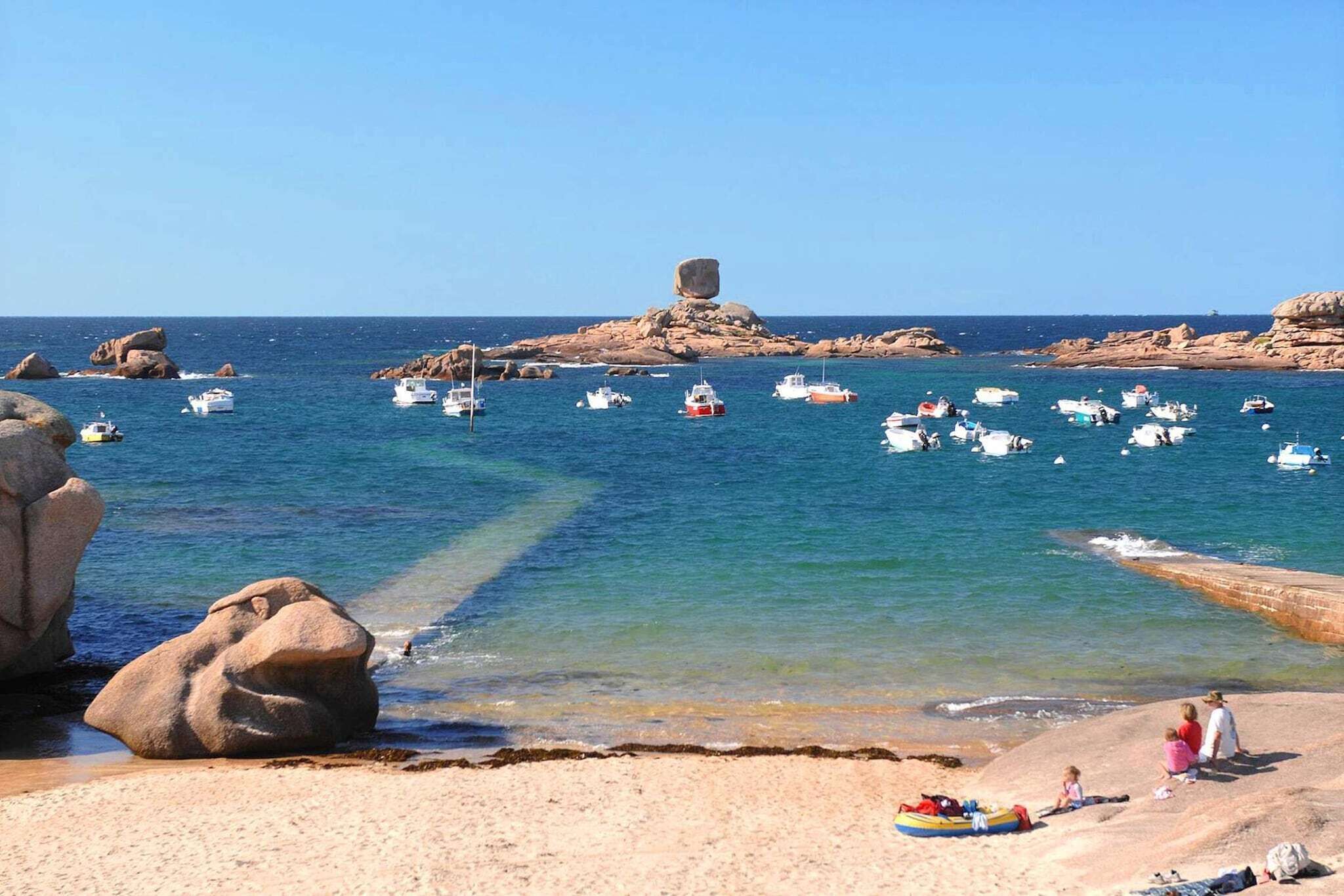 A coastal scene with boats on the water, rocky outcrops, and a sandy beach with people.