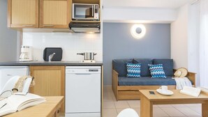 Ein kompakter Wohnraum mit Küchenzeile, Essbereich und einer Sitzecke mit Sofa und Kissen.