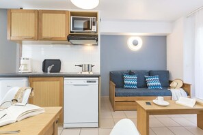 Ein kompakter Wohnraum mit Küchenzeile, Essbereich und einer Sitzecke mit Sofa und Kissen.
