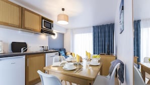 Et kompakt køkken med moderne hårde hvidevarer, et spiseområde med et bord dækket til morgenmad, og udsigt udendørs gennem et vindue.