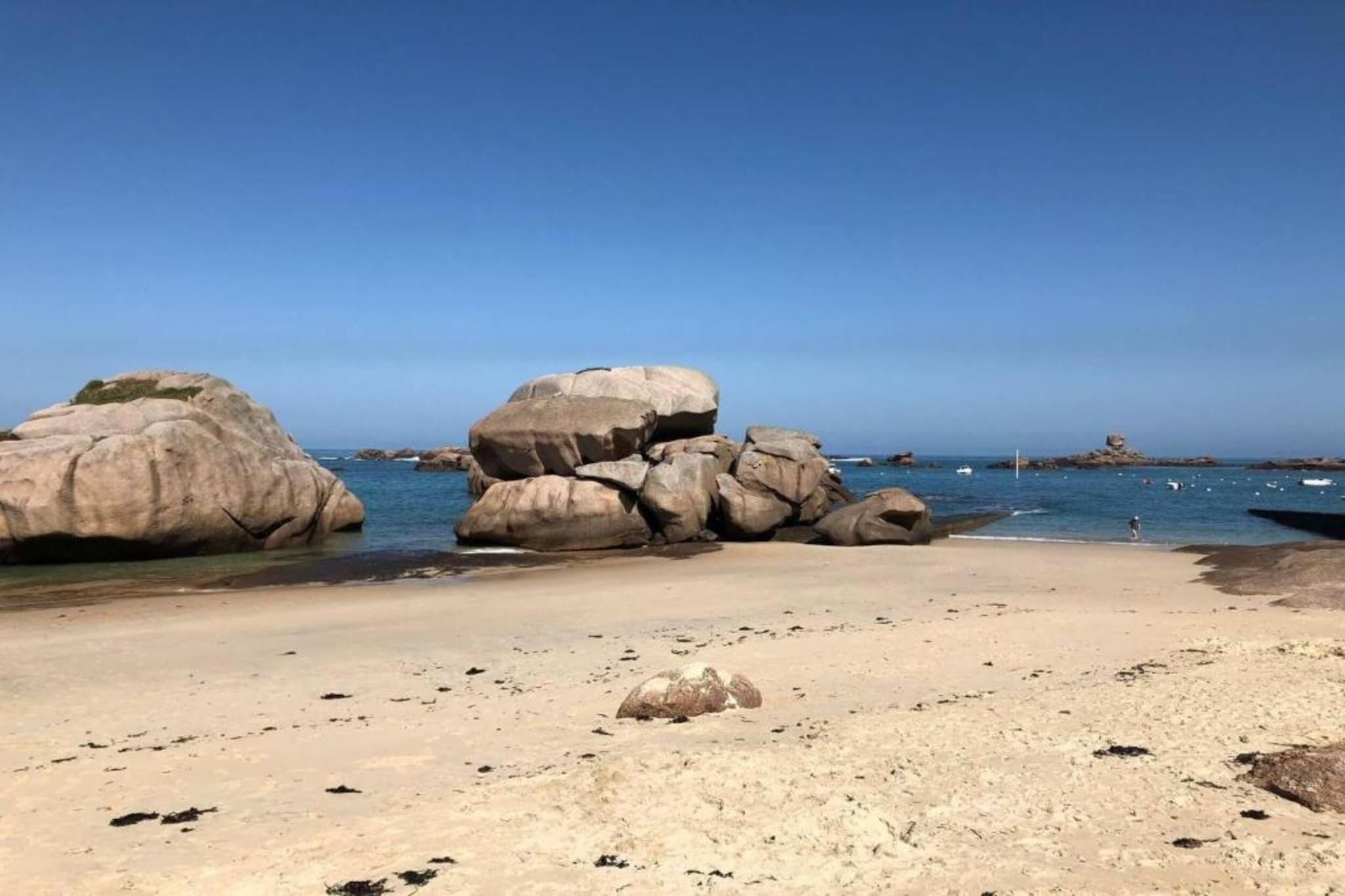 Een strand met grote rotsen en helderblauw water.