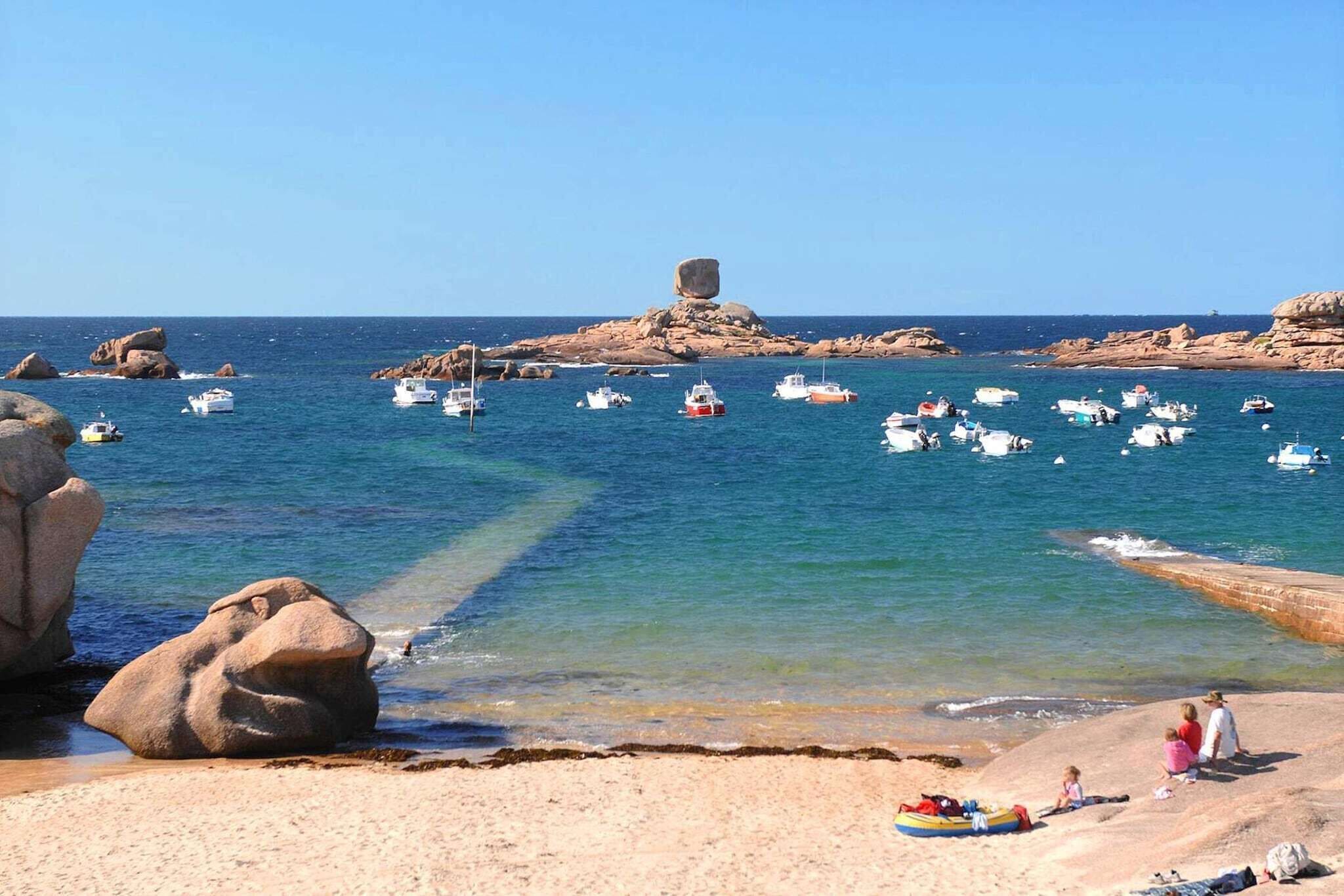 A coastal scene with boats on the water, rocky outcrops, and a sandy beach with people.