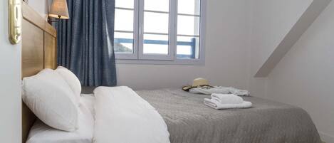 A bedroom with a bed, pillows, a window, and a lamp.