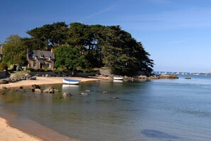 A coastal scene with a house, a beach, and boats.