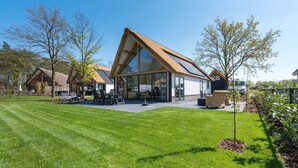 A modern house with a large glass facade, a sloped roof, and a well-maintained lawn. - Holiday Home in Netherlands Pond View (Baarle-Nassau)