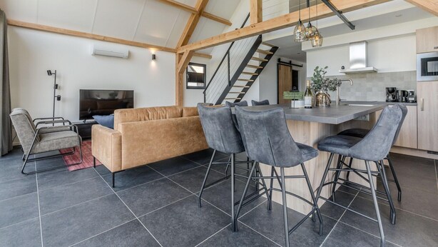 A modern kitchen with a bar area, a sofa, and a TV. - Holiday Home in Netherlands Pond View (Baarle-Nassau)