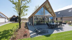 A modern house with a large glass conservatory, a patio with outdoor furniture, and a well-maintained lawn. - Holiday Home in Netherlands Pond View (Baarle-Nassau)