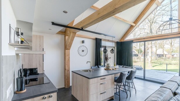 Una cocina moderna con una isla central, vigas de madera y un amplio ventanal corredera que da a un espacio exterior.