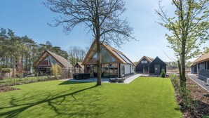 Una casa moderna con un amplio ventanal, un césped cuidado y una terraza de madera.