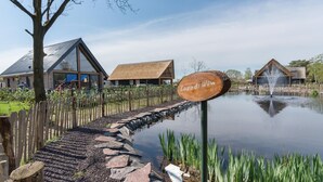 Un letrero de madera con la inscripción "Lago di Vinci", un estanque con un sendero de piedra y edificios con tejados inclinados.