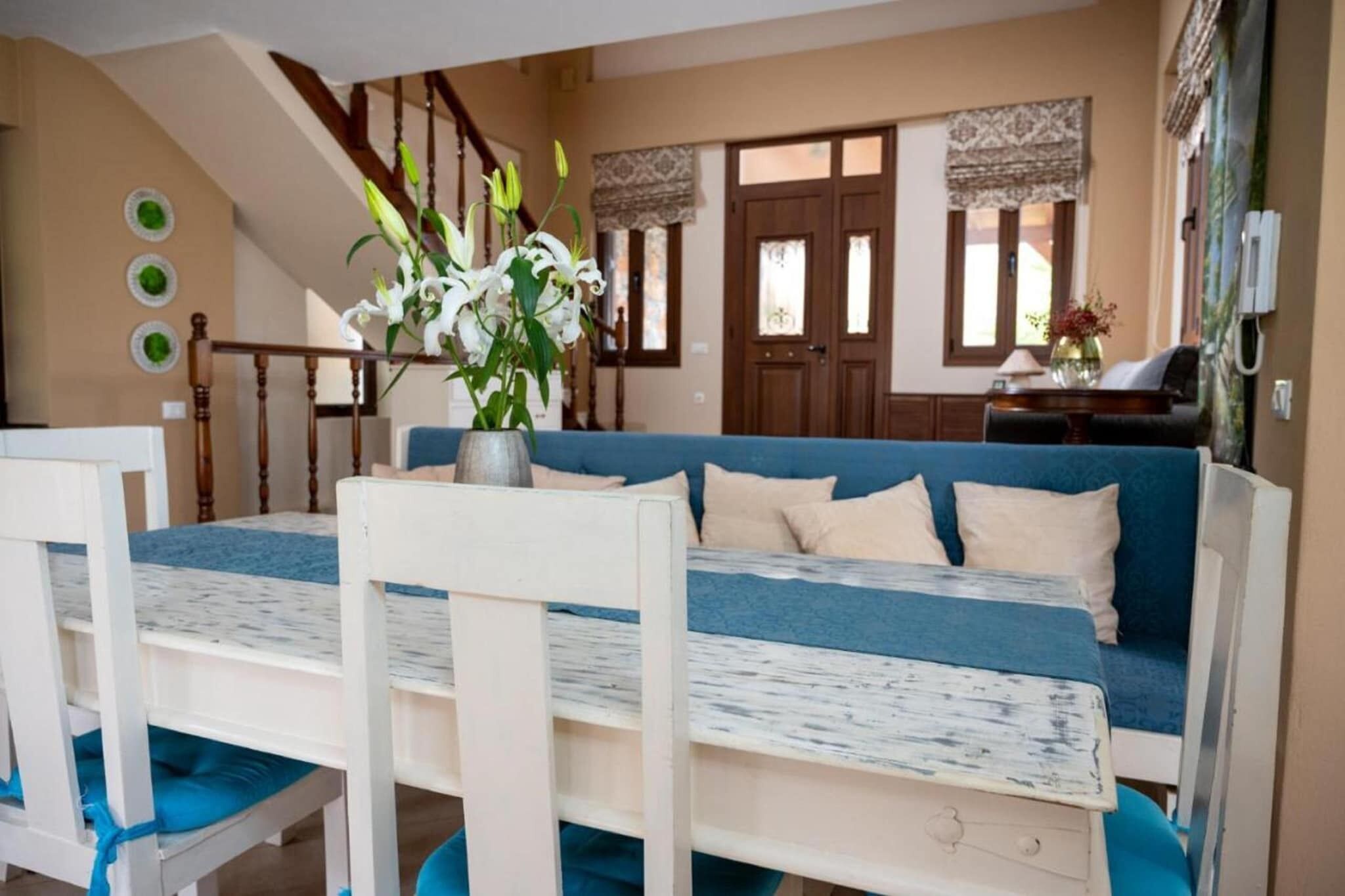 Ein gemütliches Wohnzimmer mit einem blauen Sofa, weißen Sesseln, einem Holztisch und einer Treppe.