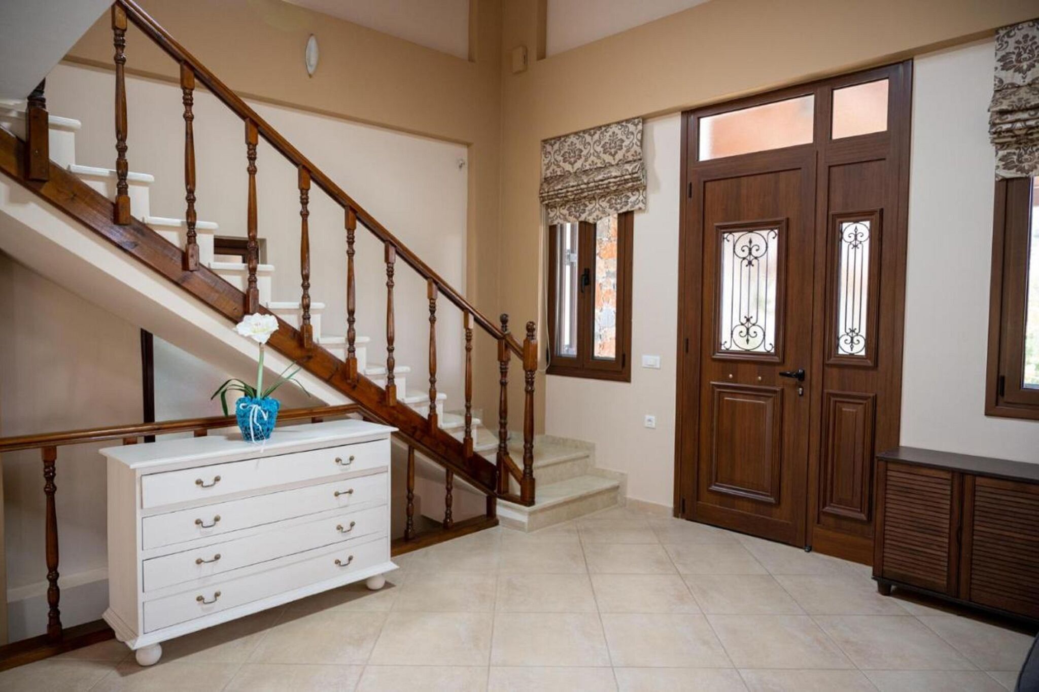 A staircase with wooden balusters, a white dresser with drawers, and a door with decorative glass panels.