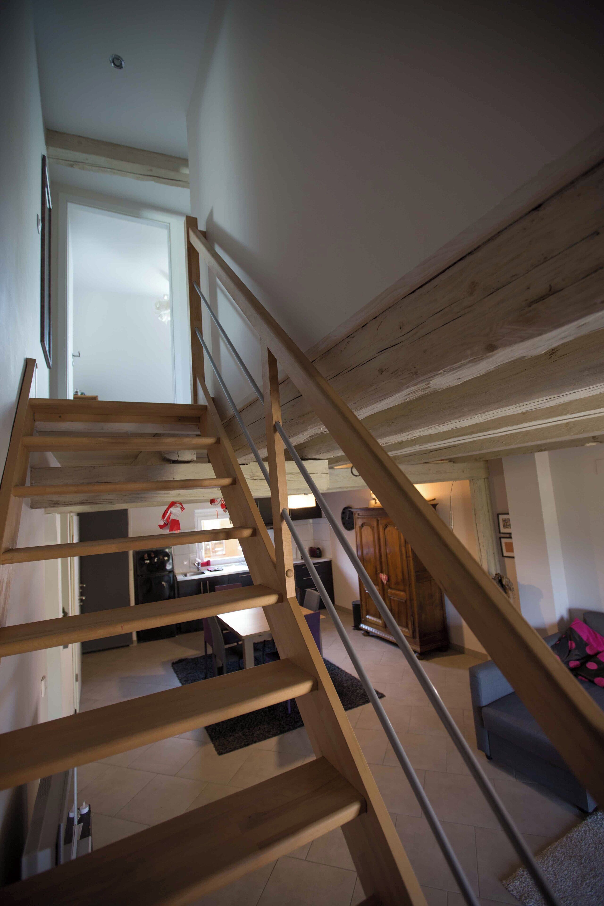A wooden staircase leading to an upper floor with a kitchen area visible below.