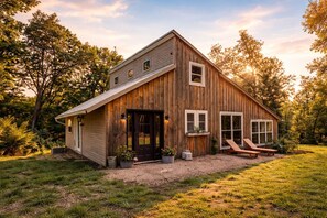 A rustic wooden cabin with a front porch, a covered entryway, and a small deck with two lounge chairs.