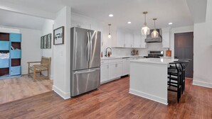 A modern kitchen with white cabinets, a stainless steel refrigerator, pendant lighting, and a wooden floor. - Adventures at Aspen Way: WHOLE HOME & 7 ACRE RETREAT (Rockbridge)