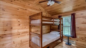 Quarto de cabana de madeira com beliche, uma mesa pequena e janela com cortinas.