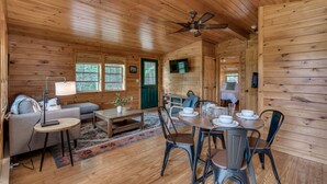 A cozy cabin interior with a dining area, sofa, and a television.