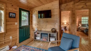A cozy cabin interior with a wooden interior, a fireplace, a television mounted on the wall, and a blue chair.