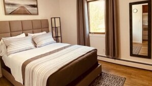 A modern bedroom with a large bed, a headboard, a bedside table, a mirror, and a window with curtains. - North Star Place Apt 8 (Fairbanks)