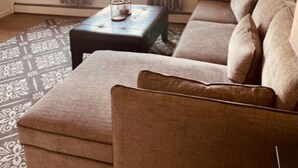 A living room with a sofa, ottoman, and a coffee table with a candle. - North Star Place Apt 8 (Fairbanks)