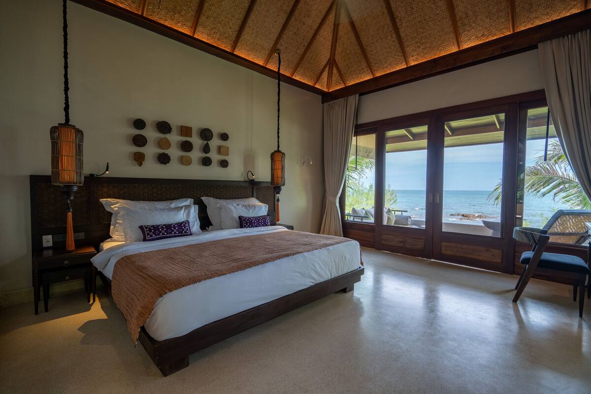 A spacious bedroom with a large bed, a view of the beach, and a tropical ceiling design.